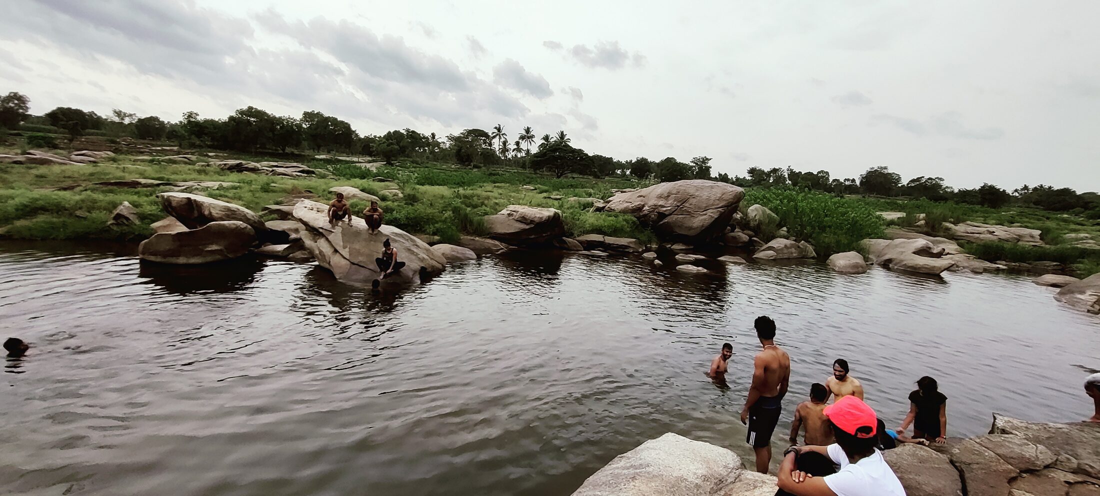 A group spending time together in a natural rocky pool surrounded by open countryside